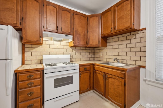 kitchen with white appliances, backsplash, tile counters, and sink