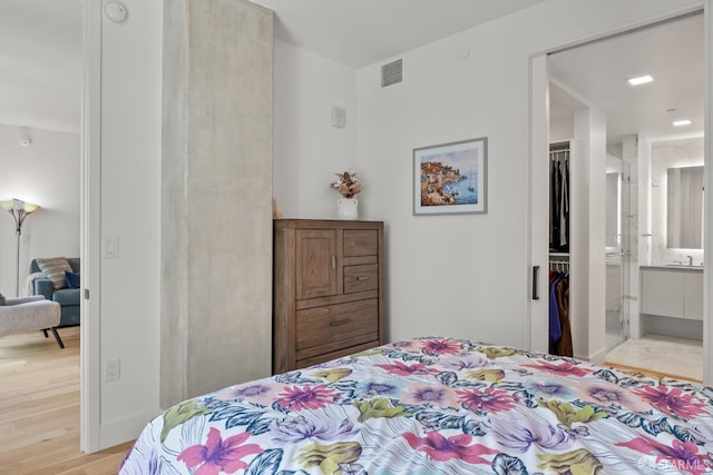 bedroom featuring ensuite bath, a closet, a spacious closet, and light hardwood / wood-style floors