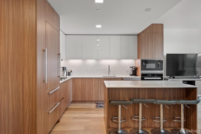 kitchen featuring stainless steel microwave, tasteful backsplash, white cabinetry, wall oven, and a breakfast bar area