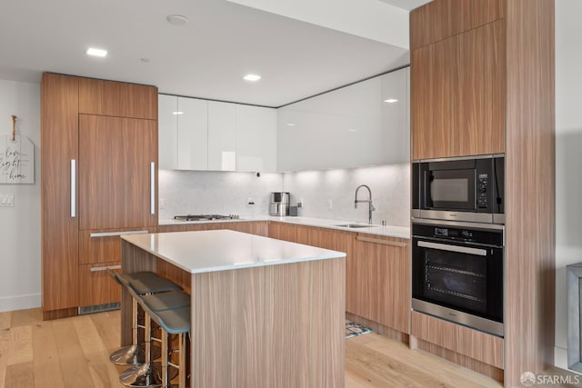 kitchen with a kitchen island, white cabinetry, built in appliances, sink, and light hardwood / wood-style flooring