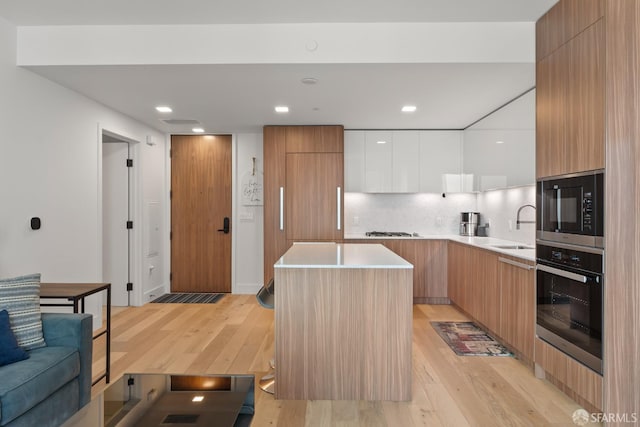 kitchen featuring wall oven, sink, built in microwave, white cabinets, and a center island