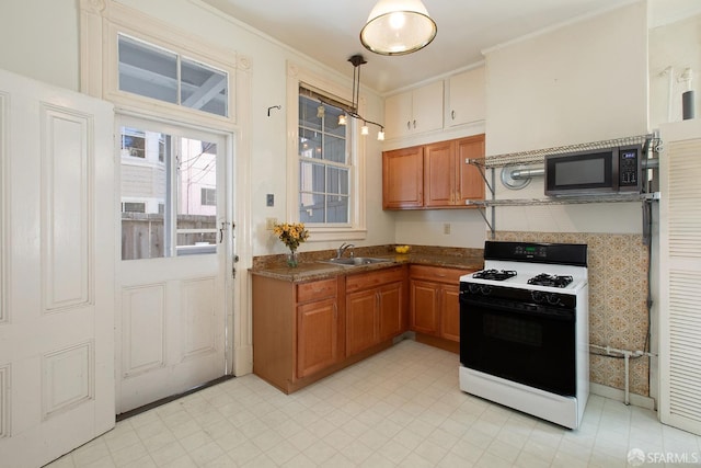 kitchen with brown cabinets, dark countertops, a sink, stainless steel microwave, and gas range oven