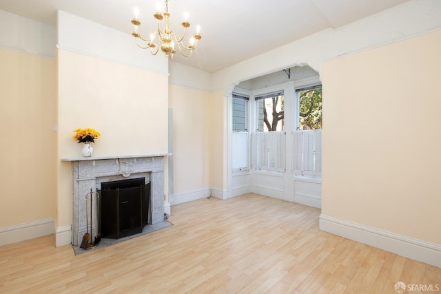 unfurnished living room with baseboards, a fireplace, light wood-type flooring, and a chandelier