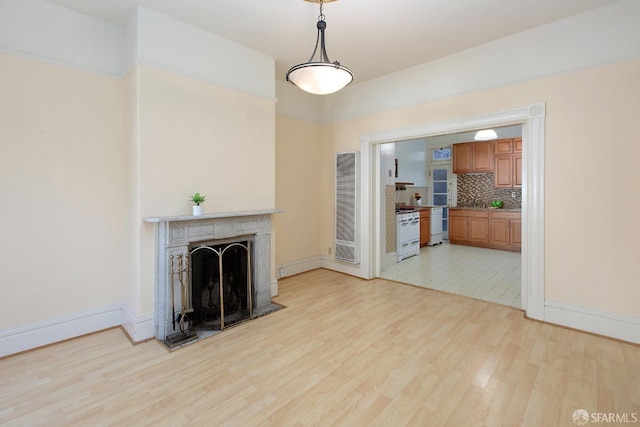 unfurnished living room with light wood-style floors, a heating unit, baseboards, and a fireplace