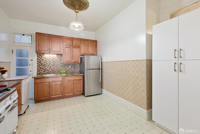 kitchen featuring freestanding refrigerator, light floors, white gas stove, brown cabinets, and a sink