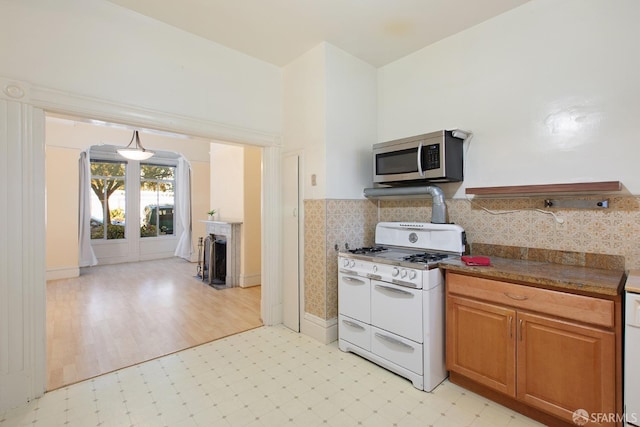 kitchen with decorative backsplash, range with two ovens, brown cabinets, stainless steel microwave, and light floors