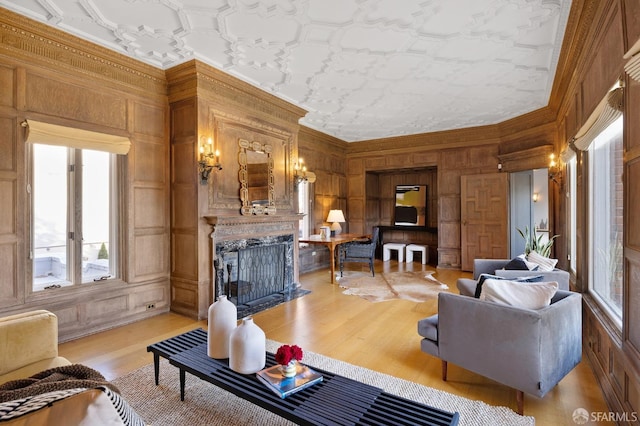 living area featuring a fireplace with flush hearth, light wood-style flooring, wooden walls, crown molding, and a decorative wall