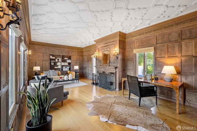 living room with wooden walls, a fireplace with flush hearth, an ornate ceiling, light wood-style floors, and crown molding