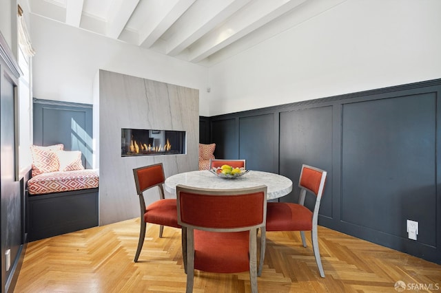 dining room with beamed ceiling, a wainscoted wall, a glass covered fireplace, and a decorative wall