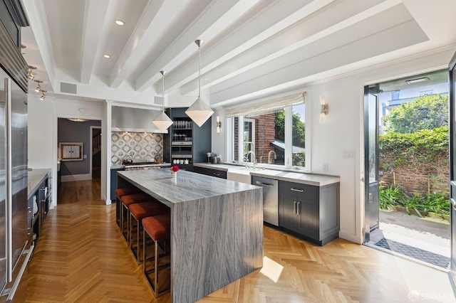 kitchen featuring beamed ceiling, a breakfast bar, stainless steel dishwasher, a center island, and wall chimney range hood