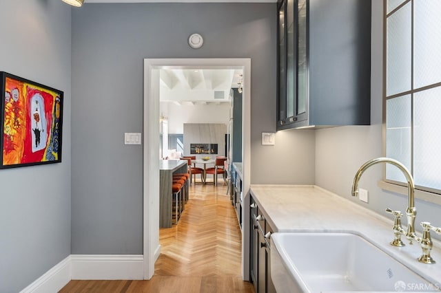 kitchen with light countertops, glass insert cabinets, baseboards, and a sink