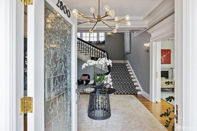 entryway with a notable chandelier, ornamental molding, wood finished floors, baseboards, and stairs