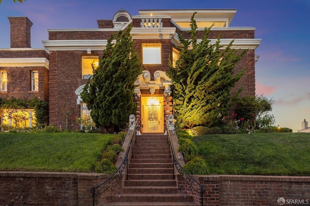 view of front of house with stairway, a lawn, and brick siding