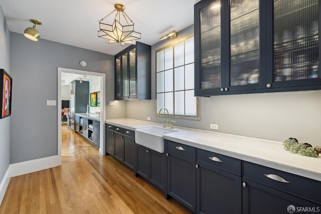 kitchen featuring glass insert cabinets, light wood-type flooring, light countertops, hanging light fixtures, and a sink