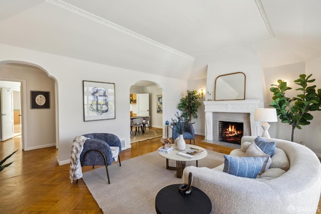 living room with arched walkways, baseboards, a lit fireplace, and ornamental molding