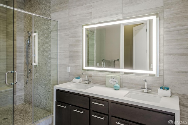 full bath with a sink, tile walls, a shower stall, and double vanity