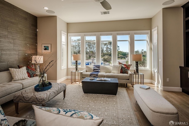 living area with baseboards, an accent wall, visible vents, and wood finished floors