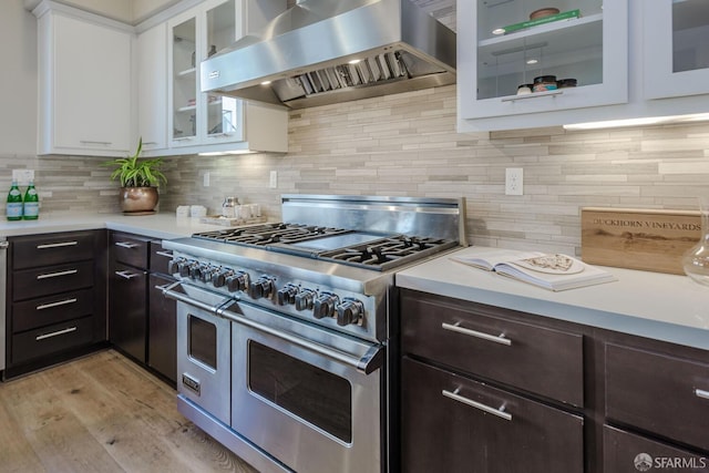 kitchen featuring range with two ovens, light countertops, white cabinetry, wall chimney range hood, and dark brown cabinets