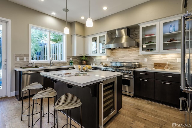 kitchen with a breakfast bar area, a sink, high quality appliances, beverage cooler, and wall chimney exhaust hood