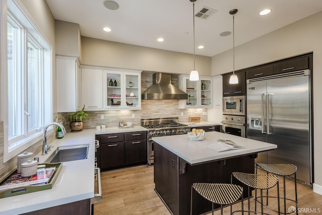 kitchen with visible vents, a kitchen island, built in appliances, wall chimney range hood, and a sink