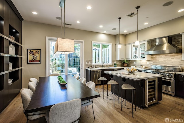 kitchen with visible vents, wine cooler, stainless steel appliances, light countertops, and wall chimney range hood