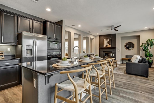 kitchen with light hardwood / wood-style flooring, a breakfast bar area, a center island with sink, and black appliances