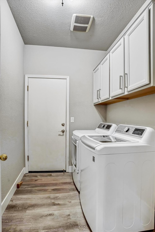 laundry area with light hardwood / wood-style flooring, washing machine and dryer, cabinets, and a textured ceiling