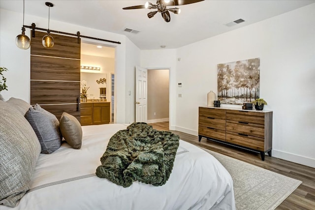 bedroom with a barn door, dark wood-type flooring, connected bathroom, and ceiling fan