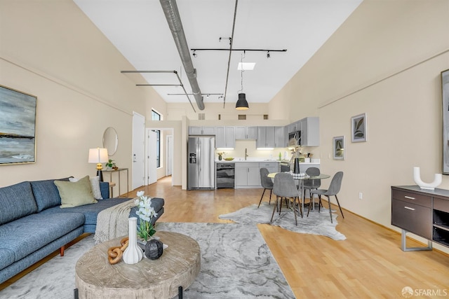 living room with a high ceiling, rail lighting, wine cooler, beam ceiling, and light hardwood / wood-style floors