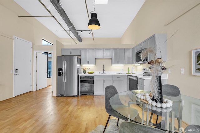 kitchen featuring light wood-type flooring, gray cabinetry, stainless steel appliances, sink, and hanging light fixtures