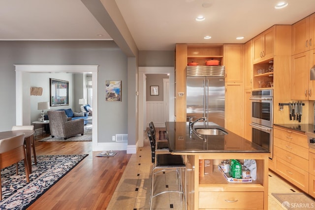 kitchen featuring open shelves, light brown cabinetry, a sink, light wood finished floors, and stainless steel appliances