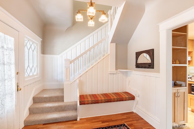 stairs with wood finished floors, a decorative wall, a notable chandelier, and a wainscoted wall