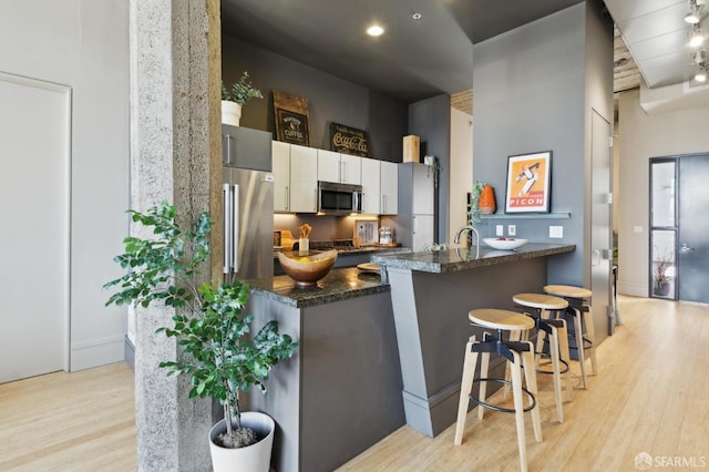 1 S Park St Unit 308, San Francisco, CA 94107 - kitchen featuring stainless steel microwave, light wood finished floors, a peninsula, a kitchen bar, and dark stone counters