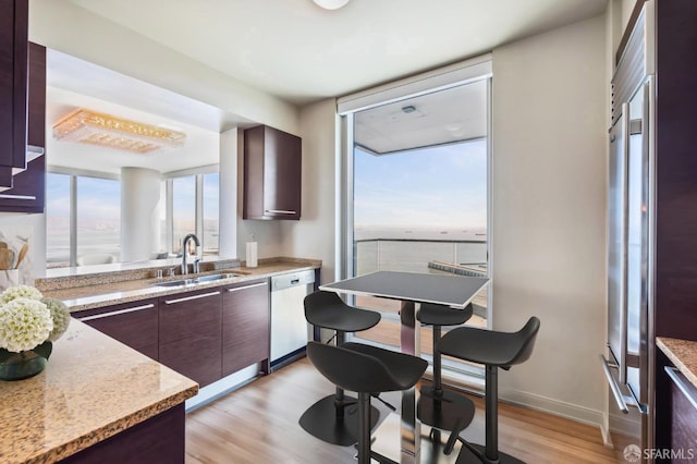 kitchen featuring light stone countertops, light wood-type flooring, dark brown cabinets, and sink