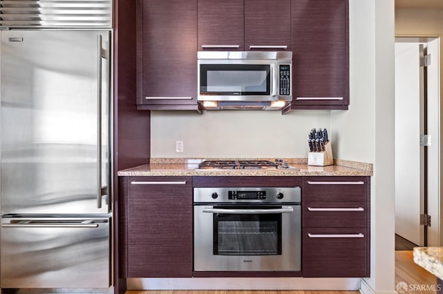 kitchen with stainless steel appliances, light hardwood / wood-style floors, and light stone countertops