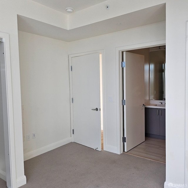 unfurnished bedroom featuring ensuite bathroom, light colored carpet, and sink