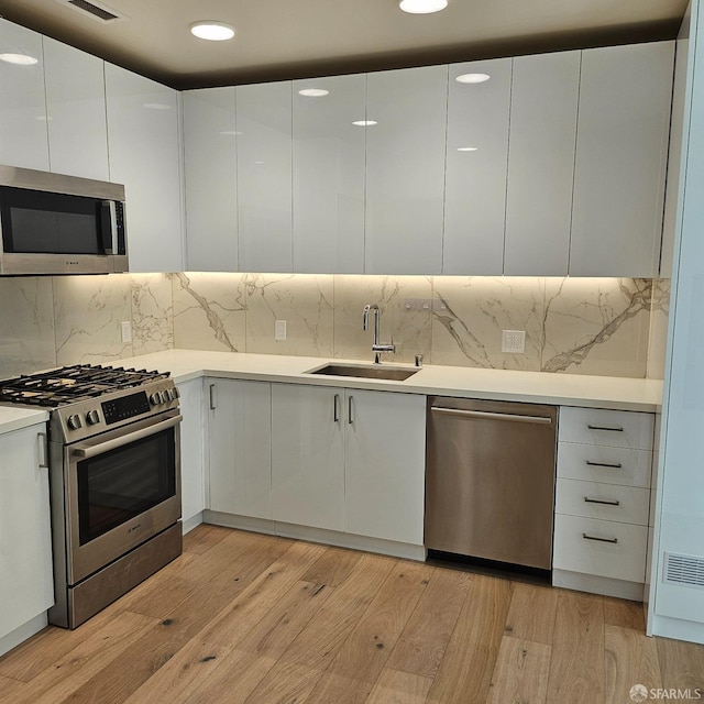 kitchen featuring white cabinetry, sink, stainless steel appliances, and light hardwood / wood-style floors