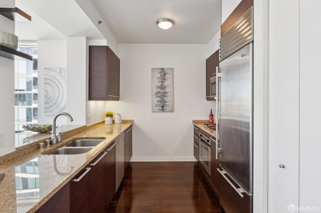 kitchen with dark wood-type flooring, dark brown cabinetry, sink, light stone counters, and appliances with stainless steel finishes