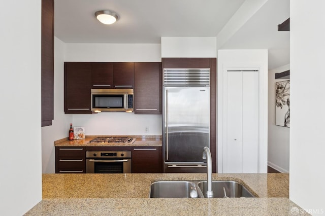 kitchen featuring stainless steel appliances, light stone countertops, sink, and dark brown cabinets