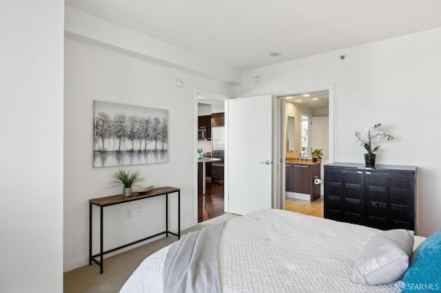 bedroom featuring stainless steel built in refrigerator, connected bathroom, and light carpet