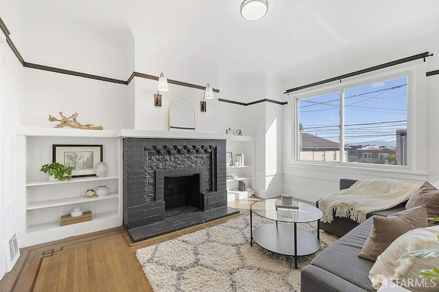 living room featuring a fireplace with raised hearth, wood finished floors, and visible vents