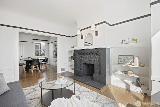 living room with a fireplace with raised hearth, wood finished floors, and visible vents