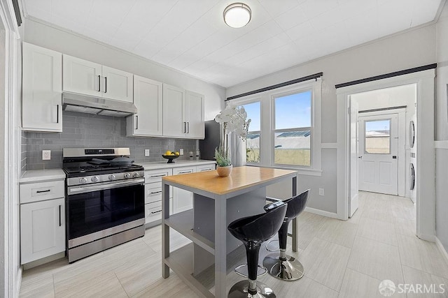 kitchen featuring stainless steel gas range oven, under cabinet range hood, white cabinetry, light countertops, and backsplash