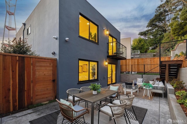 back house at dusk with a balcony, an outdoor hangout area, and a patio area