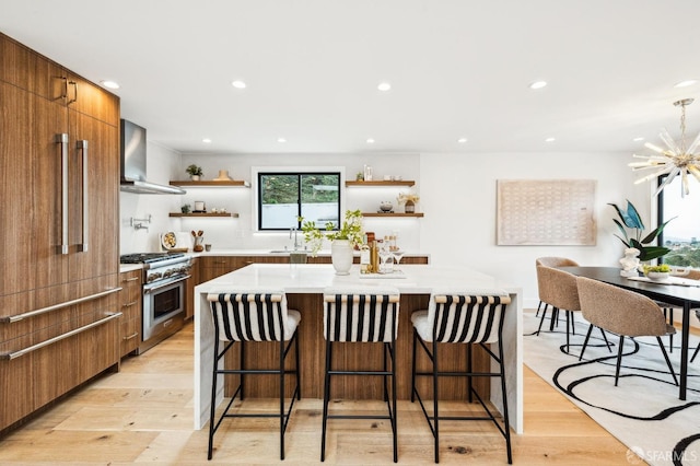 kitchen featuring wall chimney exhaust hood, high end range, a kitchen bar, and light hardwood / wood-style flooring