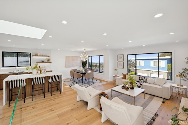 living room featuring a skylight, sink, light hardwood / wood-style flooring, and a notable chandelier