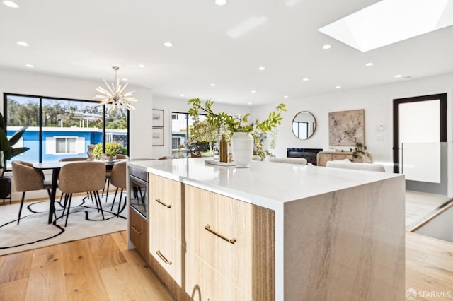 kitchen featuring stainless steel microwave, decorative light fixtures, a large island, a notable chandelier, and light wood-type flooring