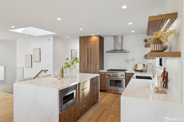 kitchen featuring sink, a center island, light wood-type flooring, stainless steel stove, and wall chimney range hood