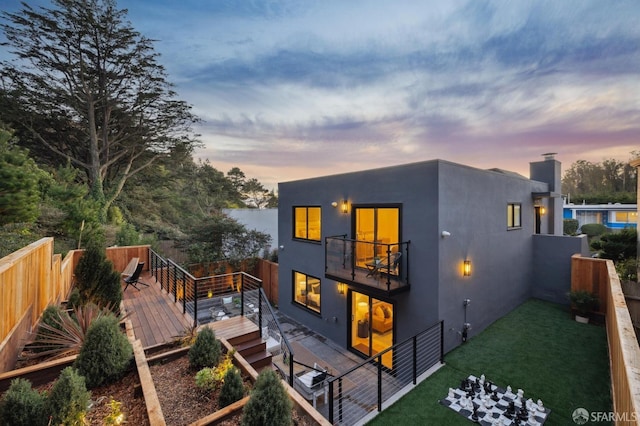 back house at dusk with a balcony, a yard, and a deck