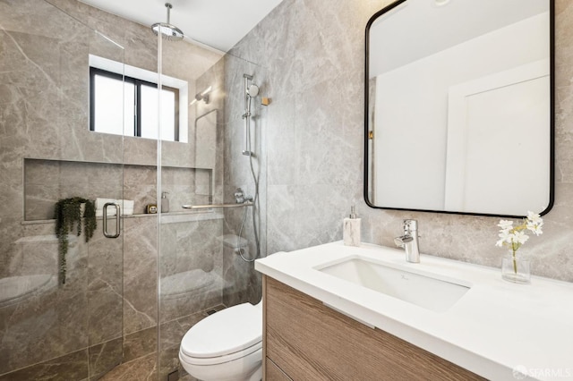 bathroom featuring vanity, toilet, a shower with door, and tile walls